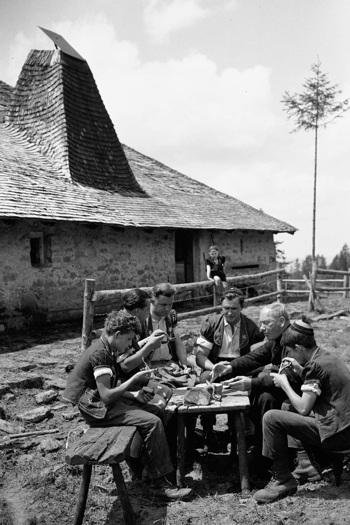 Die Sennen teilen ihre Mahlzeit mit Pfarrer Kolly oberhalb Châtel-Saint-Denis, Mitte des 20. Jahrhunderts © Glasson-Musée gruérien