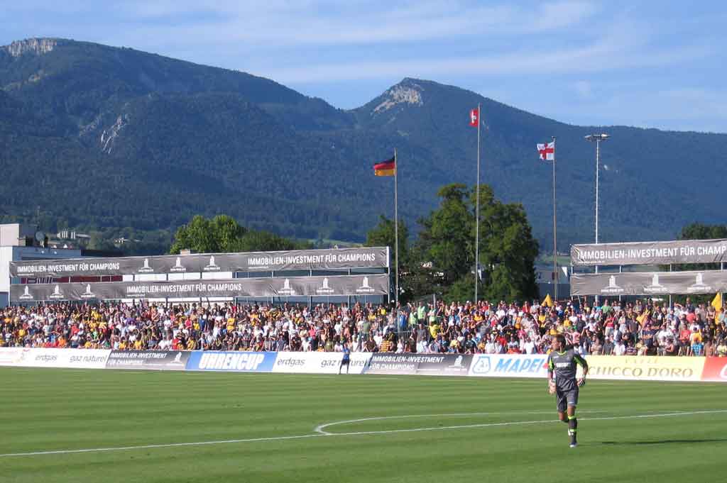 Spielfeld, Stehplätze gegenüber der Tribüne, Landesflaggen der Teilnehmerteams und das Juragebirge © Karin Janz, 2011