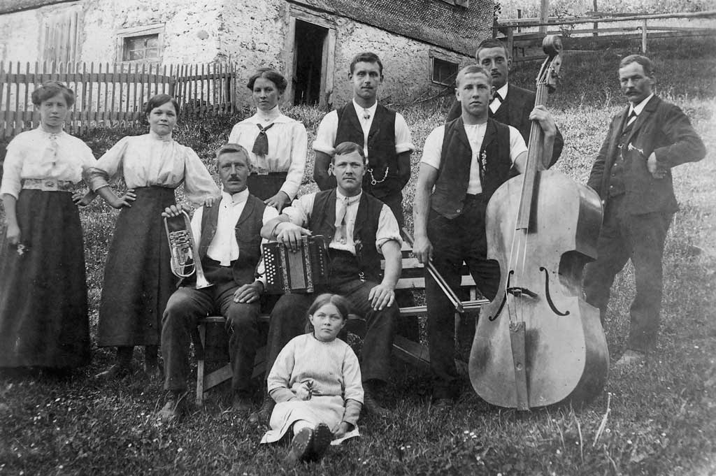 Hausmusik mit Trompete, Schwyzerörgeli und Bassgeige vor einem Heimwesen in Obwalden, um 1920 © Paul Enz, Giswil