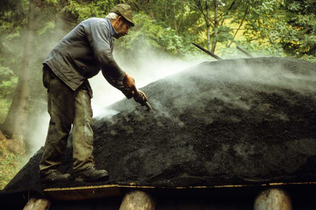 The charcoal producer regulates the ongoing charring process by poking air holes in the pile, between 1980 and 2005 © Paul Duss, Romoos