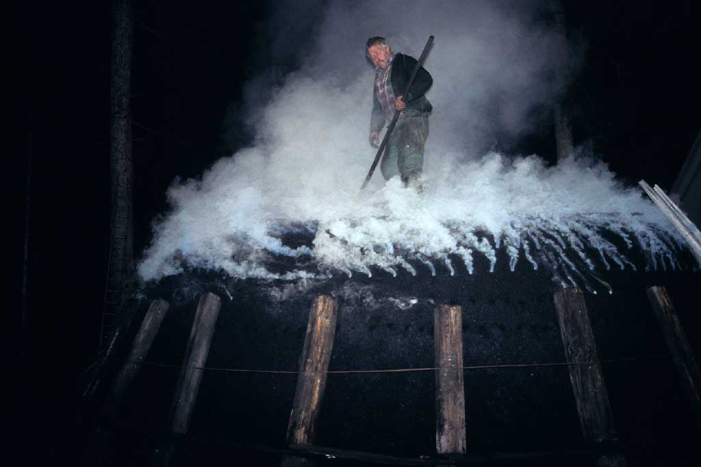 Every few hours, the charcoal producer 'feeds' the pile by throwing in glowing coal embers, between 1980 and 2005 © Paul Duss, Romoos