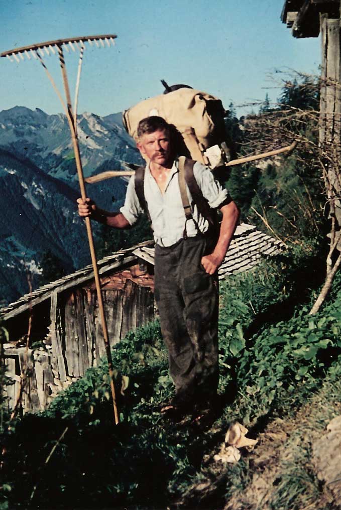 Muni d’un sac à dos, d’un râteau et de sa faux, un paysan est prêt à monter aux Planggen. Vers 1952 © Xaver Föhn-Gasser, Ibach (SZ)