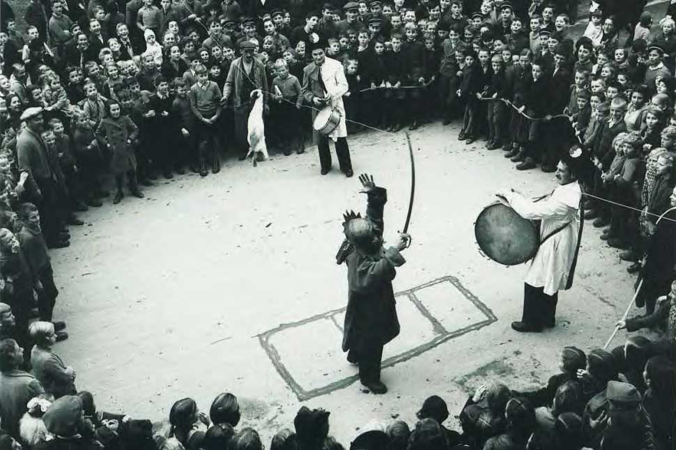 In tambur ed in pauchist accumpognan la figura mascrada, plazza da la chasa communala 1938 © Sammlung Ernst Brunner, Schweizerisches Institut für Volkskunde, Basel